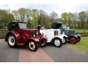 Tre veteran-lantbruksmaskiner i rött, vitt och grått uppradade utomhus.